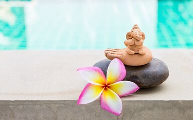 Clay Ganesh sculpture on stone with beautiful plumeria flower over blurred water background, outdoor day light, peaceful and happiness concept