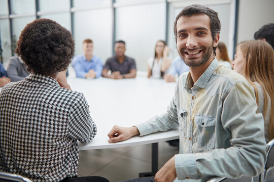 Smiling business group of office workers, executive board members or employees looking at camera sitting at conference table