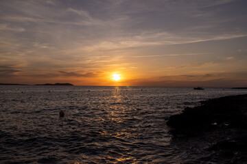 Photo of the beach at sunset on the town of Sant Antoni de Portmany on the island of Ibiza in the Balearic Islands Spain with the ocean waves and the sun reflecting on the water