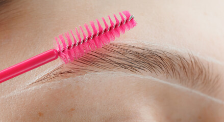 Correction of brow hair. Master brushes eyebrows to woman in beauty salon