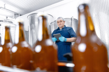 Factory worker with tablet computer control production line with bottles beer in brewery. Concept modern food industry banner