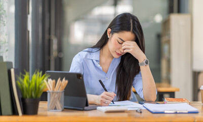 Portrait of tired young business Asian woman work with documents tax laptop computer in office. Sad, unhappy, Worried, Depression, or employee life stress concept
