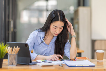 Fototapeta premium Portrait of tired young business Asian woman work with documents tax laptop computer in office. Sad, unhappy, Worried, Depression, or employee life stress concept 