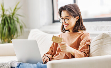 cheerful woman is engaged in online shopping side on sofa with laptop and bank card at home.