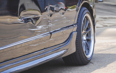 Focus at damaged scratch on surface of black car parked on the street after accident in perspective side view 