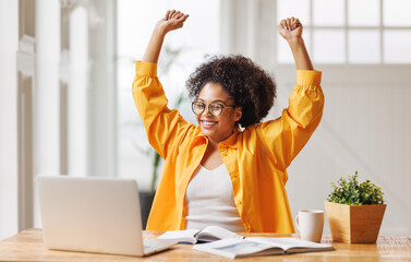 Joyful   business woman freelancer  entrepreneur smiling and rejoices in victory while sitting at desk   and working at laptop   after finishing project  in home office