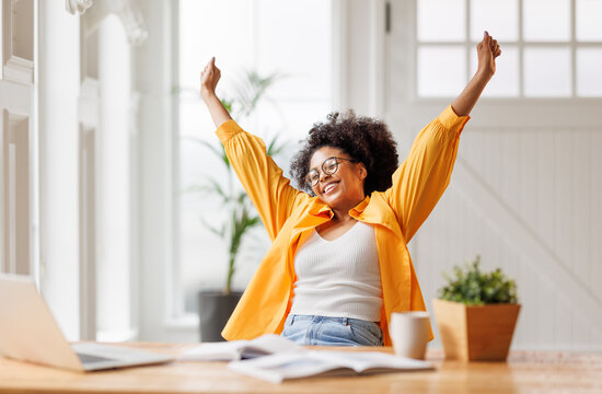 Joyful   business woman freelancer  entrepreneur smiling and rejoices in victory while sitting at desk   and working at laptop   after finishing project  in home office