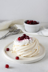 Bizet cake with cream and berries on a light plate. Cranberries in a light vase in the background. Spoons on the table. Light background