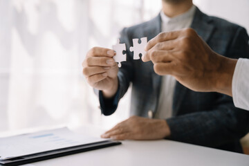 Business team work holding two jigsaw connecting couple puzzle piece for matching to goals target, success and start up new project in office, businessman concept.