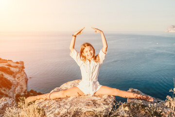 Happy smiling teen girl balerina performs stretching exercises splits on the beach during a beautiful sunset, enjoying a sunny summer day. © panophotograph