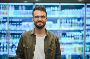 Man with a beard buys a beer in the alcohol department of a supermarket . Handsome man chooses a beer bottle in the store and communicates on a smartphone.Shopping in a supermarket