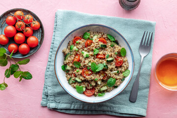 Quinoa tabbouleh salad in a bowl, a healthy dinner with tomatoes and mint, overhead flat lay shot on a pink background