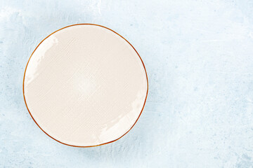 An empty white plate with a gold rim, overhead flat lay shot on a slate background, with copy space