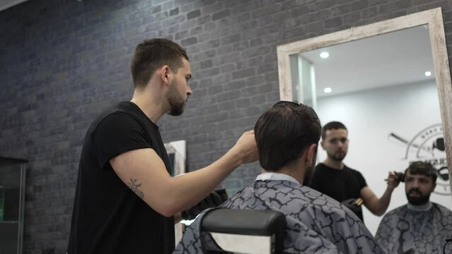 Video of a barber cutting the sideburns and doing a gradient to his client with a hair clipper and cleaning him with a small brush.