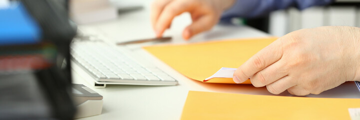 Closeup of man hands opening yellow padded envelope with letter at table. Receiving registered mail...