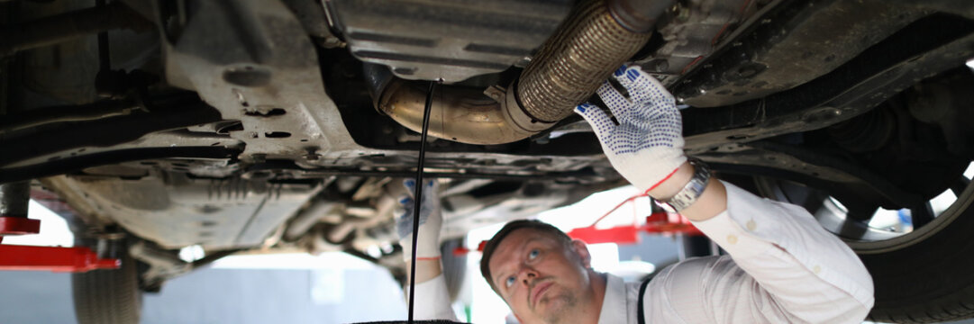 Handsome auto mechanic checks undercarriage of car at service station. Male worker fixing problem with machine concept
