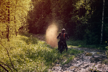 motorcycle racer on enduro sports motorcycle rides on a muddy road with puddles with splashes in...