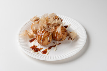 Takoyaki Chinese octopus balls , garnished with cheese sauce, soy sauce and Katsuobushi, photographed closeup on white table 