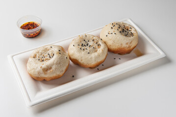 Shengjian mantou, fried shanghai sandwich stuffed with pork and jelly, photographed up close on white table 
