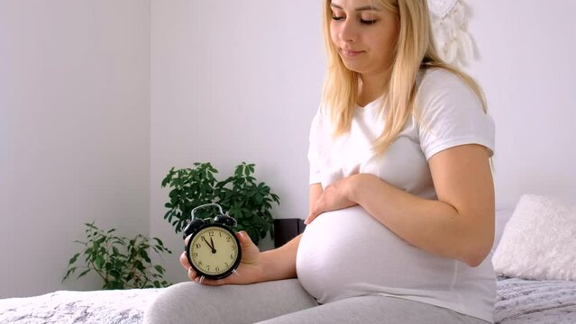 A pregnant woman holds a watch in her hands. Selective focus.