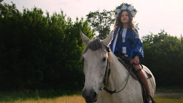 A young girl, in a beautiful Ukrainian national dress, rides a white horse.