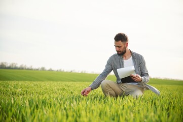 With notepad in hands. Handsome young man is on agricultural field