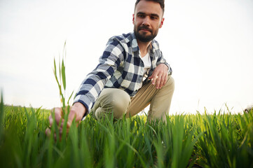 Naklejka na ściany i meble View from below. Sitting and checking quality of the wheat. Handsome young man is on agricultural field