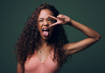 Tongue out, wink and peace by gen z girl in studio with hand, sign and gesture on green background....