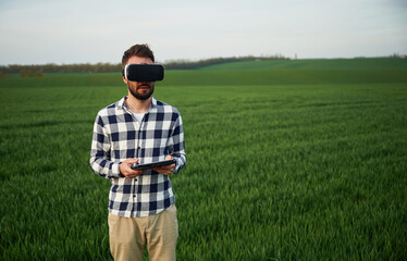 In virtual reality glasses. Handsome young man is on agricultural field