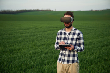 In virtual reality glasses. Handsome young man is on agricultural field - obrazy, fototapety, plakaty