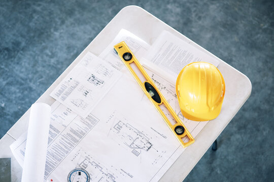Blueprint, building and project for construction above, planning or engineering equipment on table at office. Top view of floor plan, hard hat and level for architecture, safety or strategy documents