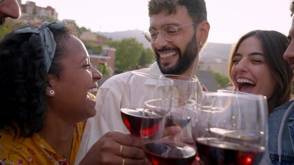 Slow motion of group of multiracial friends toasting with red wine and celebrating party on restaurant terrace. Young people laughing hugging having fun outdoors. Boys and girls enjoying in summer.