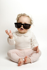 Smiling baby girl wearing sunglasses. Adorable toddler sits  on white background. Happy childhood concept. Infant portrait