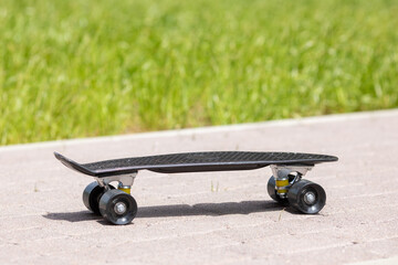 Skateboard on the grey sidewalk. Side view of skate board staying outside in summer morning. Sporty skateboard for extreme riding and tricks. Street sports concept.