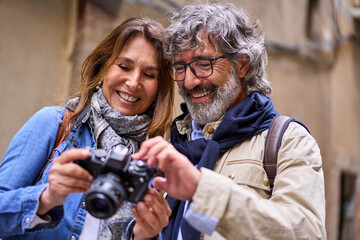 Close up of smiling retired couple holding and looking at camera photos. Mature pensioner tourist people sightseeing on vacation. Two happy people in love enjoying a weekend getaway together. 