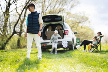 Teenager boy against family with car open trunk on picnic.