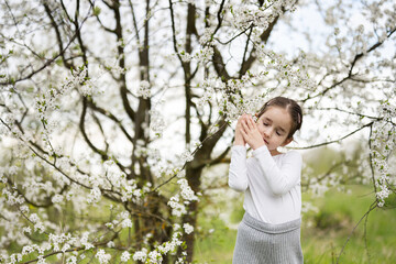 Portrait of preschool girl against white blloming tree in spring.