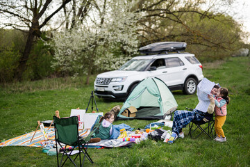 Mother hold europe map, with children sit on chair against car on picnic.