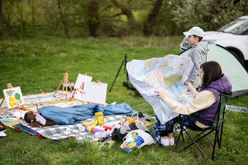 Mother hold europe map, with children sit on chair against car on picnic.