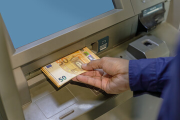 A man's hand extracting euros from an ATM.