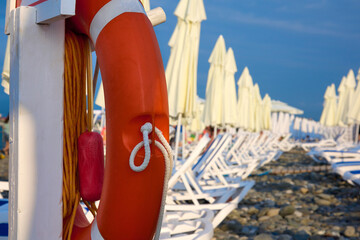 Lounge chairs with umbrellas lined up on clear rocky shore by sea against blue sky on beautiful...