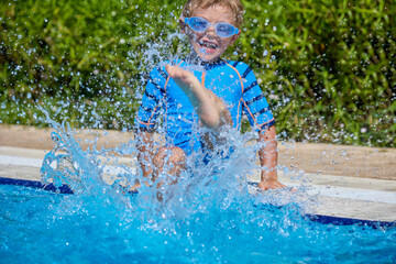 Wet splashes fly in opposite direction from play of cheerful boy in outdoor pool against the...