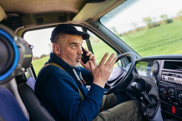 Mature truck driver using mobile phone while driving transport vehicle.