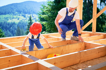 Father with toddler son building wooden frame house. Man worker instructing his son on measurement...
