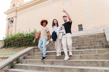 Group of diverse multiethnic student people walking together downstairs of the campus, talking, pointing and smiling. Young teenage asian woman with two male friends having a conversation after class