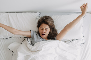 Top view of yawning and stretching asian woman just wake up on the bed.