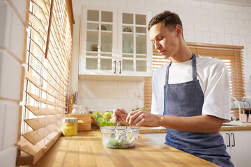 young man preparing vegetable salad in the kitchen - obrazy, fototapety, plakaty
