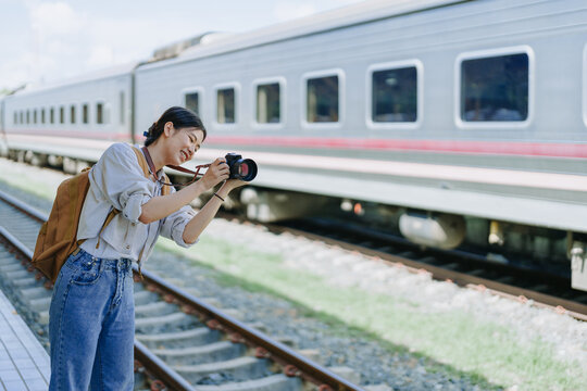 Asian teenage girl traveling using a camera take a photo to capture memories while waiting for a train at the station.