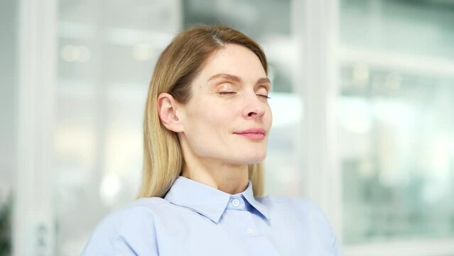 Close up of calm woman relaxing with her eyes closed in a modern office. Portrait of a happy female resting, breathing deeply. Positive mature businesswoman enjoys the work of the air conditioner
