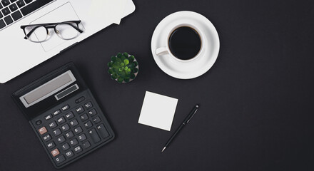 Laptop, glasses, coffee cup and calculator on a black background, top view.